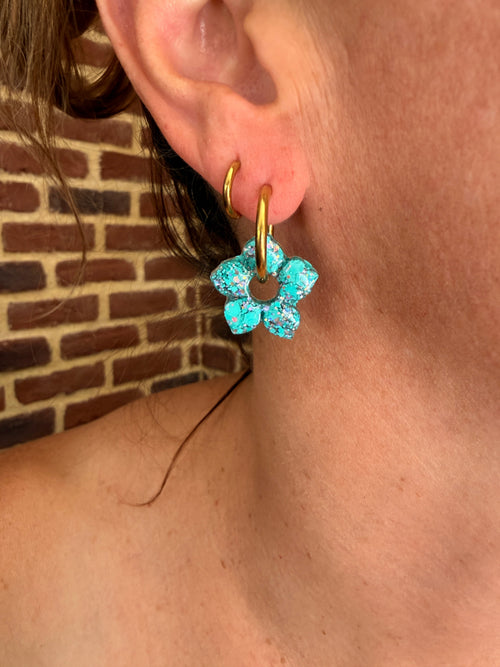 Pampille fleur à pétales pointus en résine turquoise portée sur une créole dorée