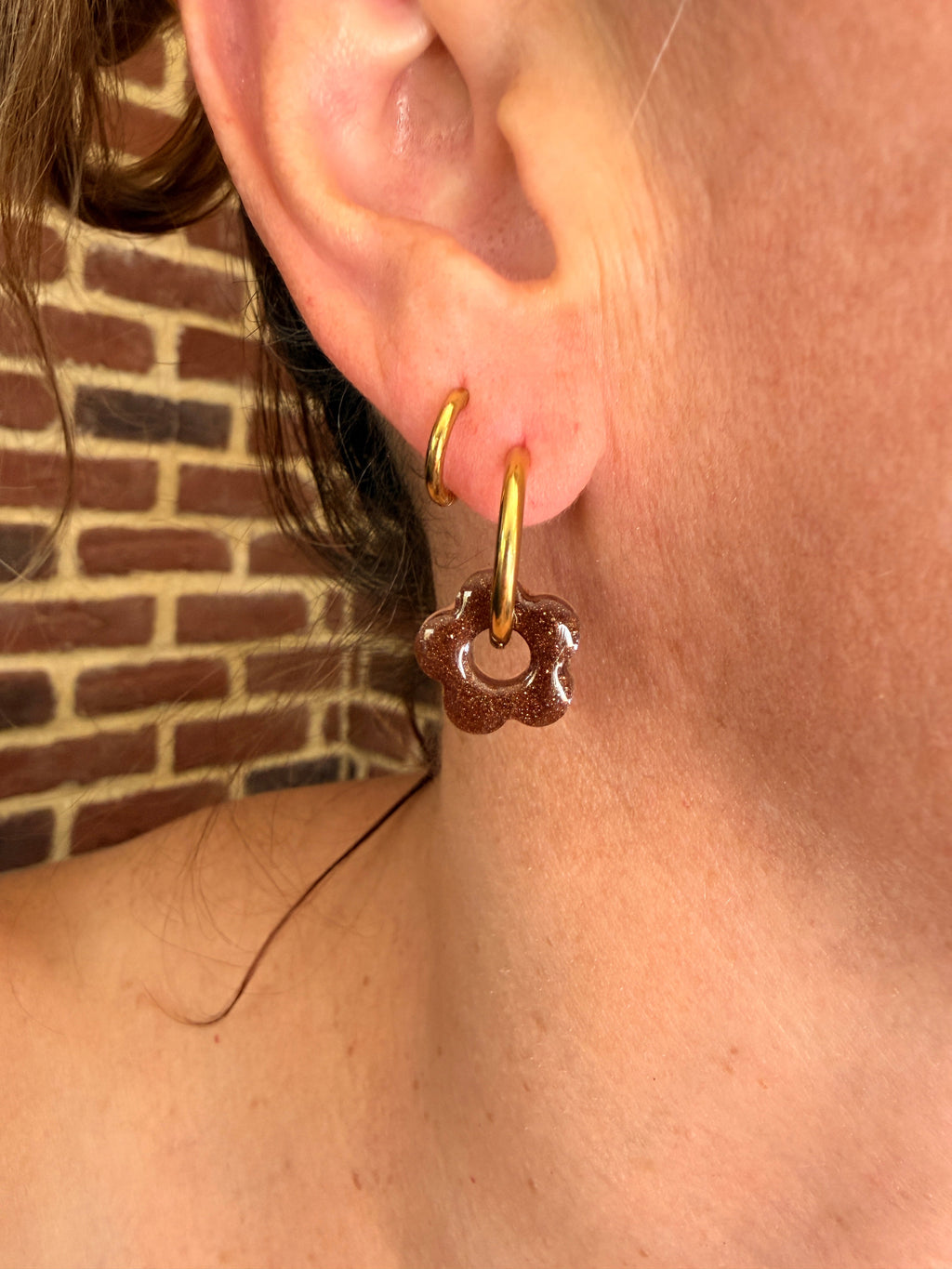 Petite pampille fleur en résine marron pailleté portée sur une créole dorée