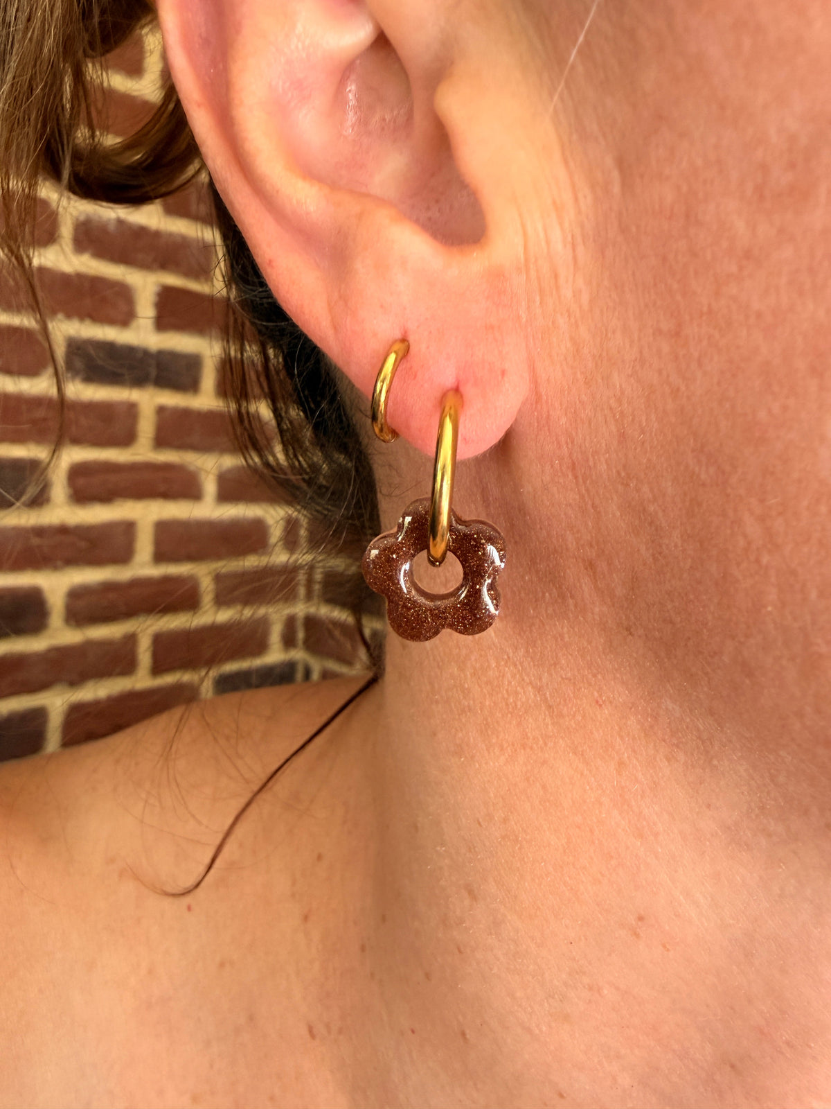 Petite pampille fleur en résine marron pailleté portée sur une créole dorée